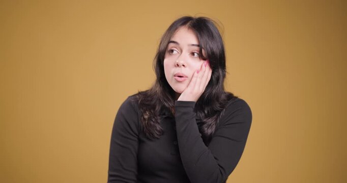 Young woman expressing shock and surprise with hand on face against a yellow background