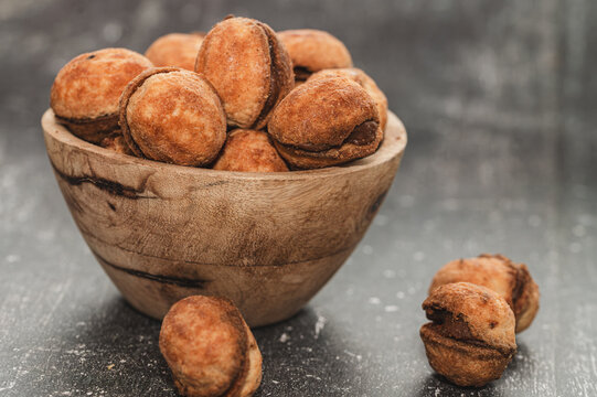 Traditional walnut shaped cookies filled with chocolate or caramel cream in a wooden bowl. Sweet homemade oreshki biscuits on a dark rustic background, popular Eastern European dessert for holiday cel