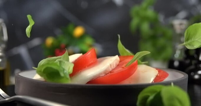 Basil leaves falling onto caprese salad on black background slow motion 1000 fps