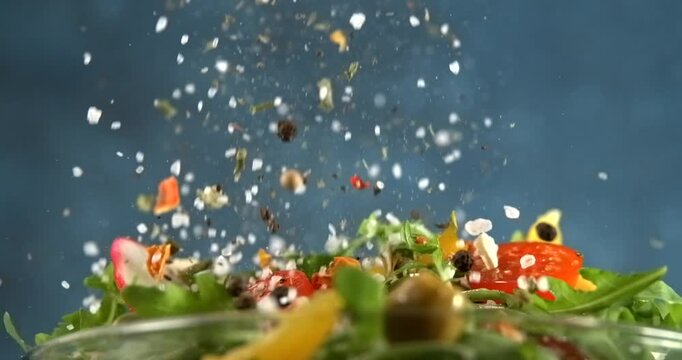 Herbs and spices falling onto fresh vegetable salad with arugula tomato cucumber and cheese in slow motion
