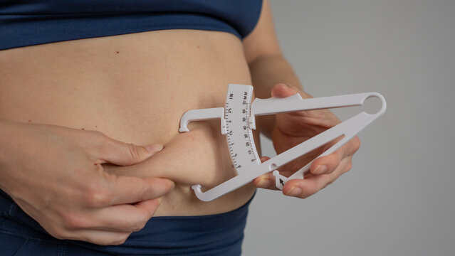 A woman measures the amount of subcutaneous fat on her abdomen using a caliper.