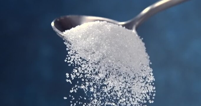 Sugar falling from a spoon in slow motion on blue background
