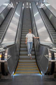 A blind woman descends an escalator in the subway.
