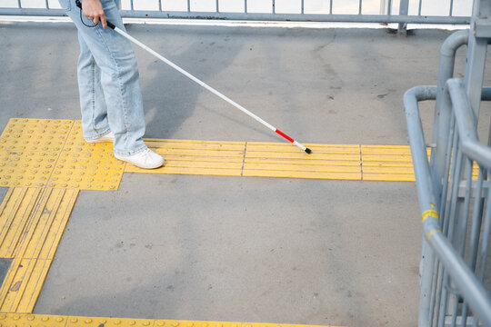 A blind woman walks using a cane and tactile tiles.