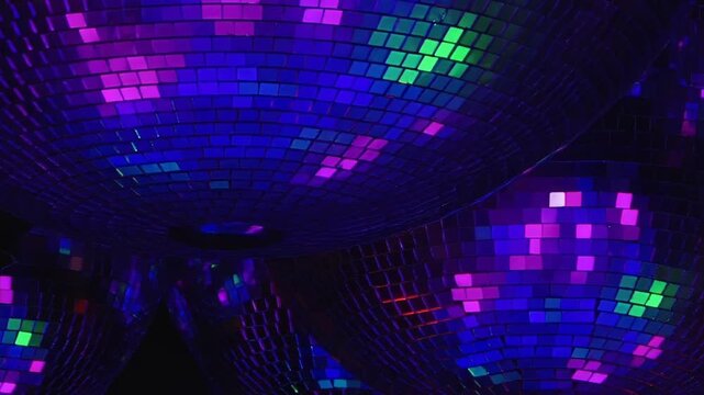 Blue and Purple Light Across a Cluster of Mirrored Disco Balls. Packed reflective spheres fill the dark interior while tiled mirror surfaces scatter changing light into shimmering abstract patterns.