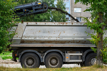 Cold milling machine conveyor discharging reclaimed asphalt pavement into a tipper dump truck during urban road reconstruction in a residential district. © Alexander Korotkov