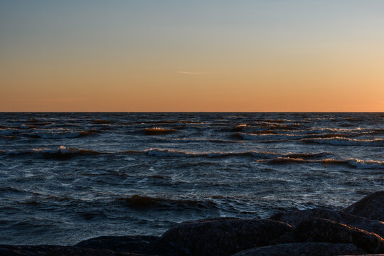 Choppy sea waves during warm sunset dusk with coastal rocks in the foreground at Baltic Sea.
