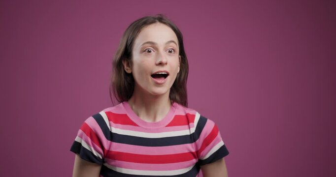 Young woman expressing surprise with wide eyes on a purple background