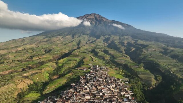 Aerial view of Kruwisan Village nestled among lush green terraced fields at the base of a majestic mountain in Kledung, Central Java, Indonesia.