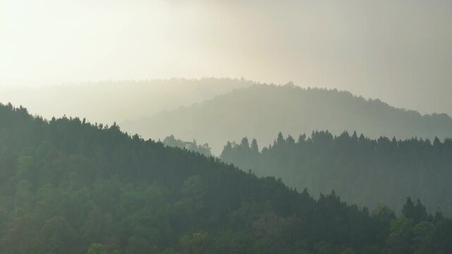 Aerial view of layered mountain ridges covered in dense forest under a soft, misty atmosphere in Sukabumi, West Java, Indonesia.