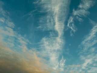 Blue sky with wispy white clouds drifting across. Warm orange hues glow near the horizon. Perfect for backgrounds, travel themes, or serene nature designs. Calm and uplifting atmosphere evokes peace © mark_gusev