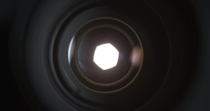 Extreme closeup of a camera lens aperture slowly opening as intense bright light emerges from behind the blades. Cinematic visual representing photography, optics, focus, exposure, illumination.