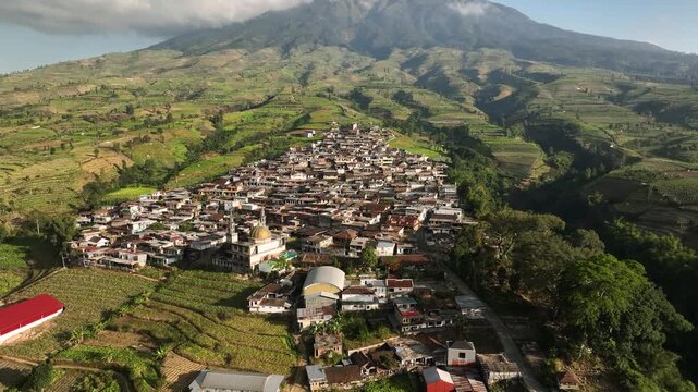 Aerial view of Kruwisan Village nestled among terraced fields with a mosque and mountain backdrop in Kledung, Central Java, Indonesia.