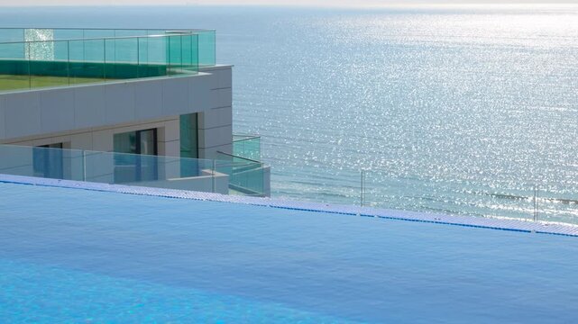 Modern luxury hotel with infinity pool overlooking the sea. Modern luxury hotel featuring an infinity pool with crystal clear blue water overlooking the sparkling sea on a sunny day