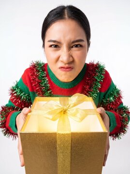 Woman presenting glowing gift box with grumpy expression in studio