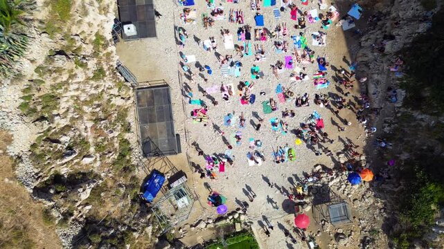 Aerial view of the crowded Lama Monachile beach in Polignano a Mare, with people sunbathing on the pebble shore surrounded by rocky cliffs in Polignano a Mare, Apulia, Italy.