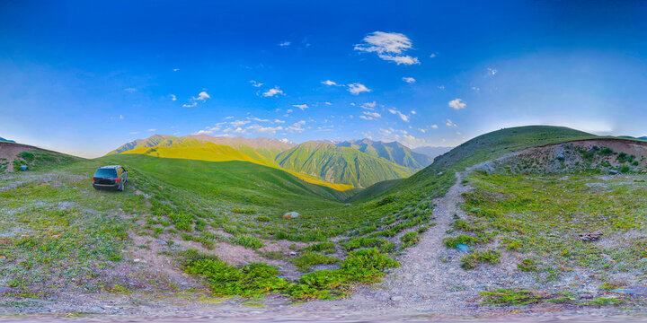 360-degree spherical panorama features a mountainous landscape in Kyrgyzstan. A dirt path winds through green hills, with a dark SUV parked on a grassy incline under a clear blue sky.