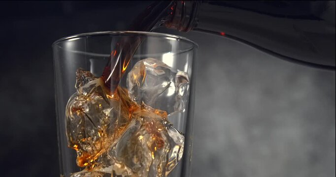 Cola type sweet fizzy drink pouring into glass with ice cubes in slow motion on black background