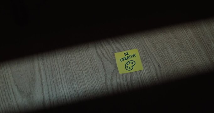 Person slides a yellow sticky note reading &ldquo;Be Creative&rdquo; with an artist palette symbol into view, representing creativity, imagination and artistic inspiration.