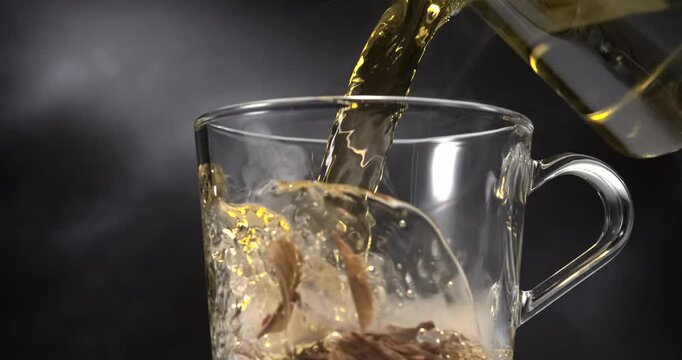 Hot green tea pouring into glass cup with tea leaves and steam in slow motion