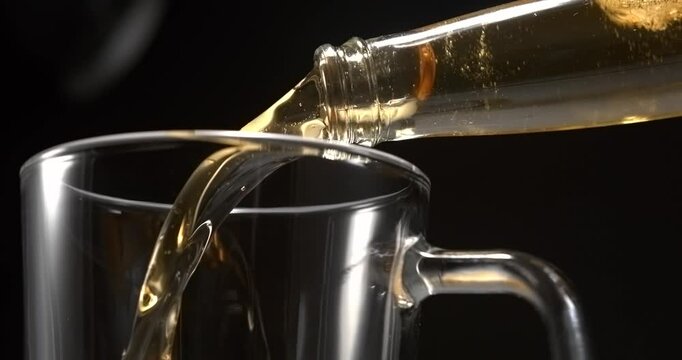 Beer pouring from glass bottle into mug in slow motion