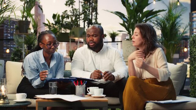 Business team discusses project documents during a rooftop brainstorming meeting, comparing notes and developing a business idea together on an elevated terrace in an economic hub.