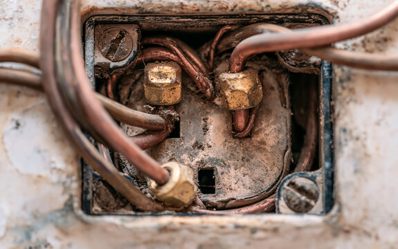 Macro view of old electrical outlet with messy wires, wire nuts. Tangled copper cables connect to dirty power socket in industrial setting. Close up of worn out electric system