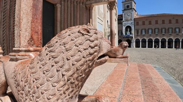 Sunlit view of Modena cathedral with its intricate facade and lion statues guarding the entrance in the historic city center of Modena city in Italy