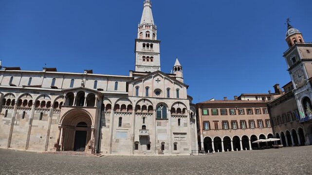 Modena Cathedral, Duomo di San Geminiano, UNESCO World Heritage site, with its Romanesque architecture and the iconic Ghirlandina Tower overseeing sunlit cobblestone piazzay of Modena city in Italy