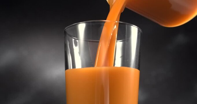 Carrot juice pouring into glass in slow motion on black background