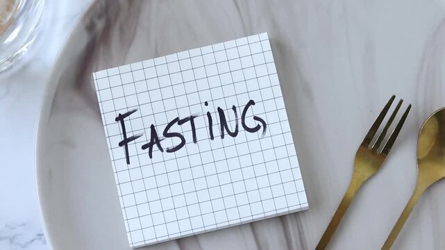 Fasting, handwritten text note on an empty plate with golden fork and spoon. Christian concept.