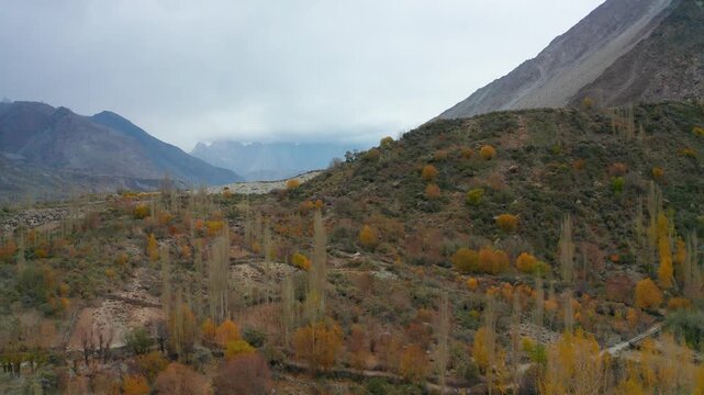 Aerial view of Sost Valley featuring colorful autumn trees, rugged mountain slopes, and a cloudy sky in Sost, Gilgit, Pakistan.