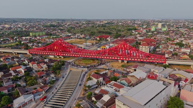 Aerial view of the red Jembatan Kereta Api Joglo railway bridge spanning over a busy roundabout and urban residential area in Surakarta, Central Java, Indonesia.