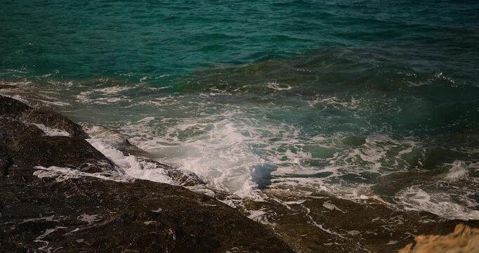 Serene turquoise ocean waves gracefully crash against rugged dark coastal rocks, creating a peaceful and captivating natural scene.