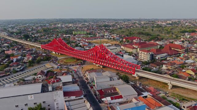 Aerial view of the red Jembatan Kereta Api Joglo railway bridge spanning over the urban landscape of Surakarta, Central Java, Indonesia.