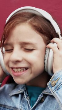 Happy redhead child listen playlist music with headphones outdoor - Technology trends - Vertical video