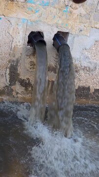 Shot of muddy rainwater pouring heavily from two plastic drainage pipes into a canal after a severe rainstorm.
