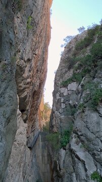 Tilt up shot of a narrow rocky gorge with steep limestone cliffs leading to an old abandoned concrete dam with stairs at Presa de Isber in Alicante, Spain.