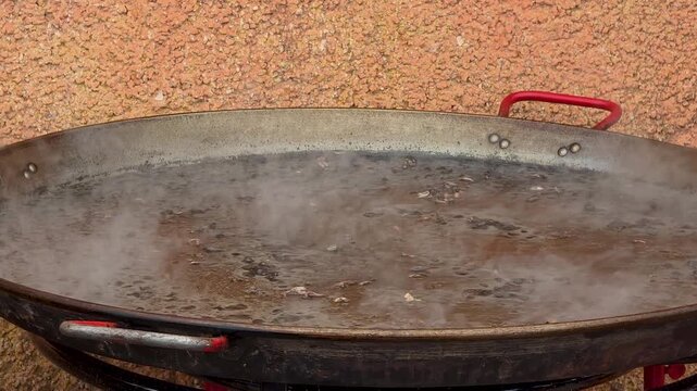 Close up shot of black fideua seafood paella boiling with steam in a huge traditional pan at Festival Gastronomic