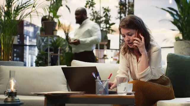 Businesswoman handles a smartphone call while typing on a laptop keyboard in a rooftop garden, talking on the phone and multitasking with the notebook as a female entrepreneur on the city rooftop.
