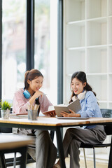 Asian female students studying and collaborating on academic projects in a modern library, sharing knowledge, researching, and preparing for exams in a university setting © David