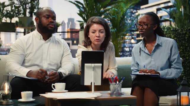 Coworkers examine a tablet display during a brainstorming session on a rooftop terrace workspace, while the team compares digital information on the device from a lounge above the enterprise hub.