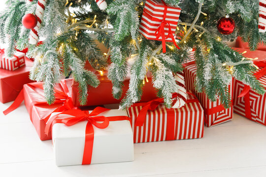 Beautiful presents, gift boxes wrapped in elegant red paper under green snowy festive Christmas tree with warm lights. Cozy winter holiday atmosphere perfect for seasonal celebrations and decor themes