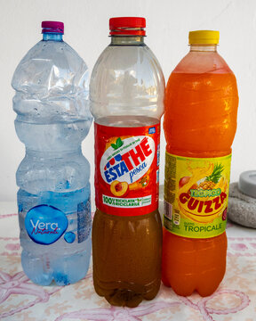 Capo d'Orlando - IT - Sep 08, 2026 : Three plastic beverage bottles stand on a patterned surface, including bottled water, peach iced tea and an orange tropical fruit drink with condensation nearby.