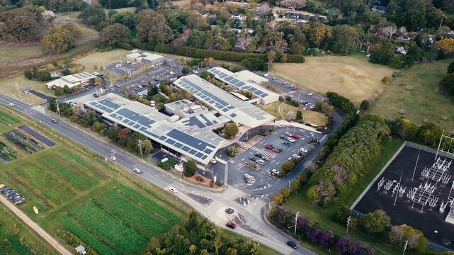 Aerial view of a hospital complex with solar panels, adjacent highway, power substation, and surrounding farmland in Byron Bay, New South Wales, Australia.