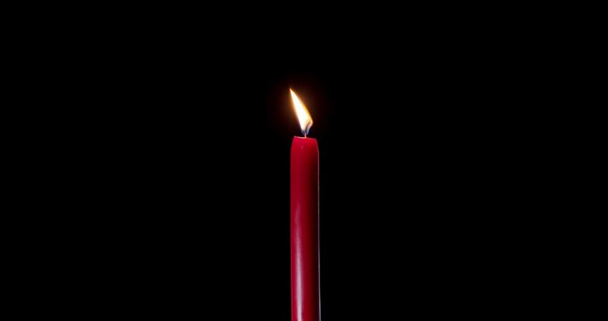 A single red candle burning on a dark, isolated background. This festive candle shines with a bright, clean flame of hope. Perfect candle for stock layouts with blending mode screen or add.