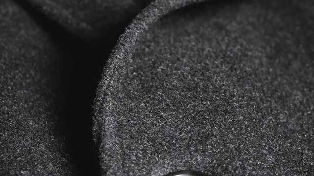 A close-up of a dark grey wool coat lapel shows high-quality winter apparel fabric, elegant black buttons, and tailoring craftsmanship highlighting professional textile weaving.