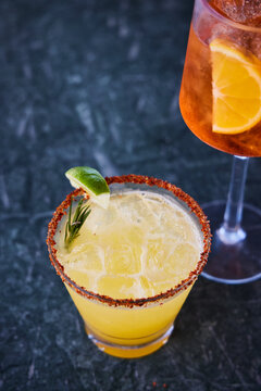 Pool drinks, margarita and Aperol Spritz over a black marbled surface.