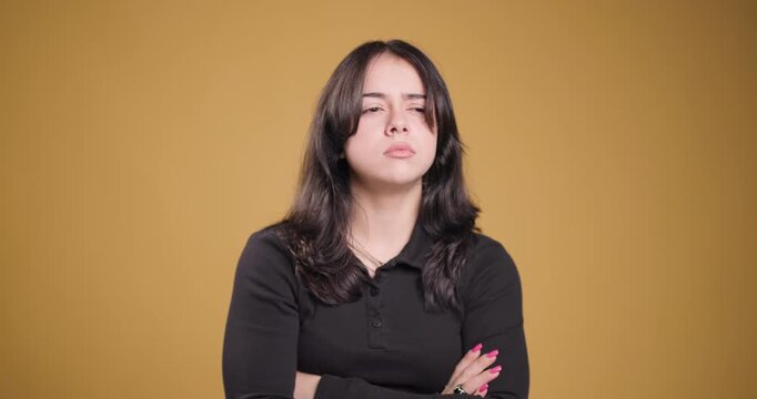 Young woman expressing discontent and frustration, arms crossed on yellow background