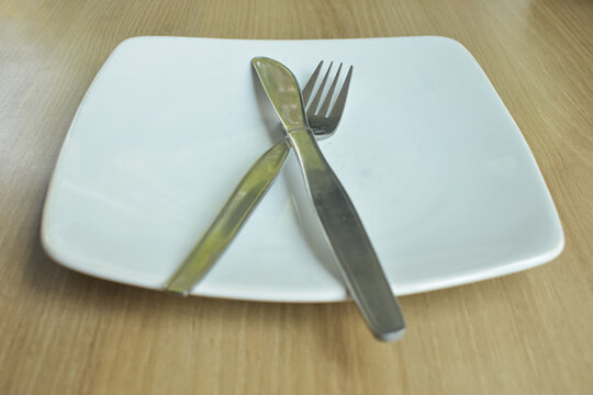 Empty White Square Plate With Fork And Knife Crossed On Wooden Table